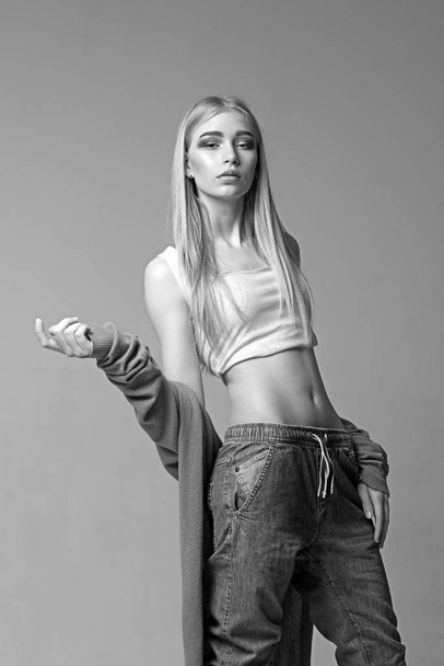 Blond girl with straight hair isolated on gray background. Young model in jeans posing in studio - Fotografie, Obrázek