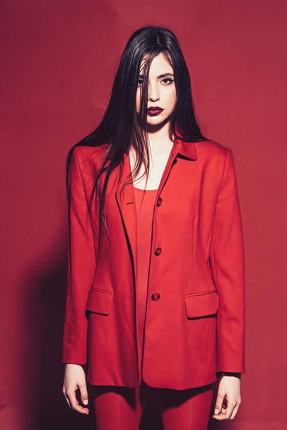 Woman with stylish makeup and long hair posing in total red outfit. Fashion concept. Girl on mysterious face in red formal jacket, red background. Lady with dark lips looking at camera. - Zdjęcie, obraz