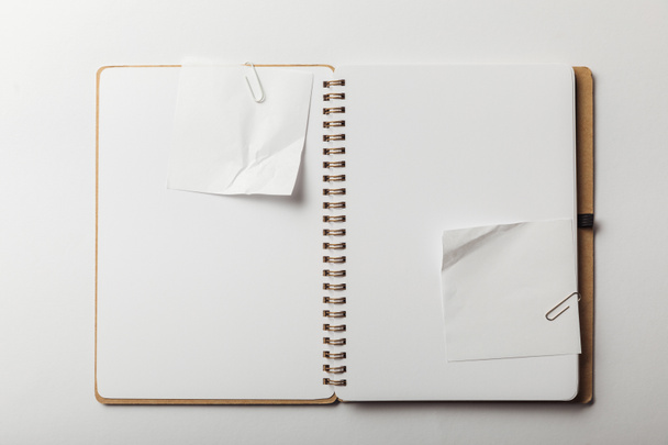 bovenaanzicht van laptop met witte kleverige nota's en paperclips op witte achtergrond - Foto, afbeelding