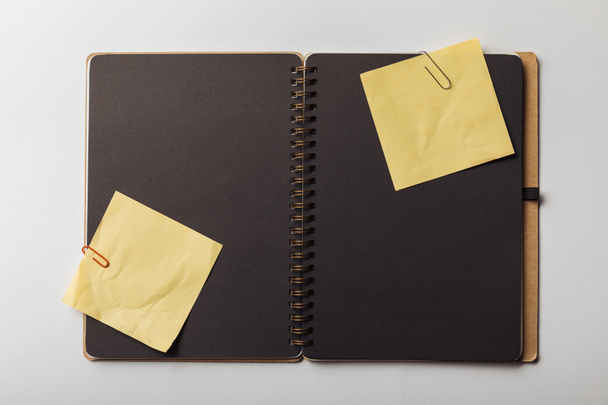 top view of opened notebook with black sheets and sticky notes with paper clips on white background - Foto, Bild