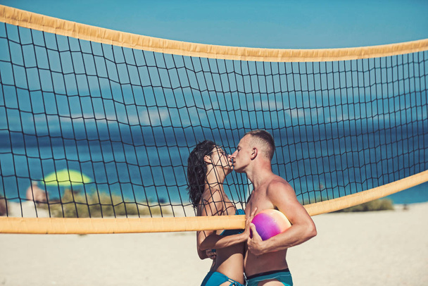 Love and flirting of couple. Sexy woman and muscular man with ball at net. Summer vacation and travel on holiday in Miami. Couple in love play volleyball on sunny beach. Sport activity and health - Photo, Image