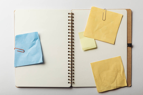 top view of opened notebook with blue and yellow sticky notes with paper clips on white background - Photo, Image