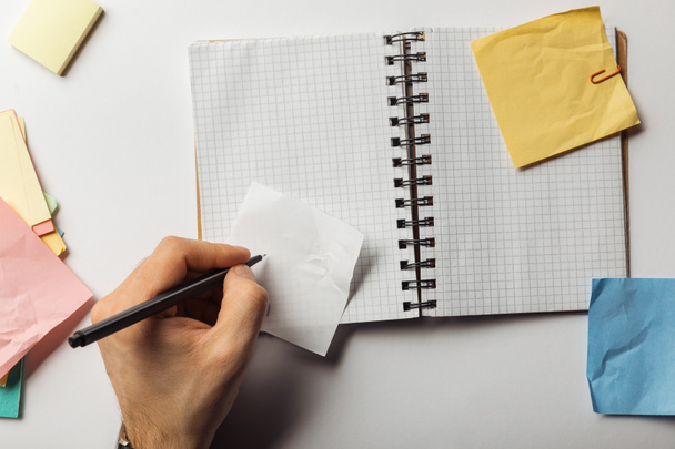 cropped view of man writing on sticky note near opened notebook  - Photo, Image