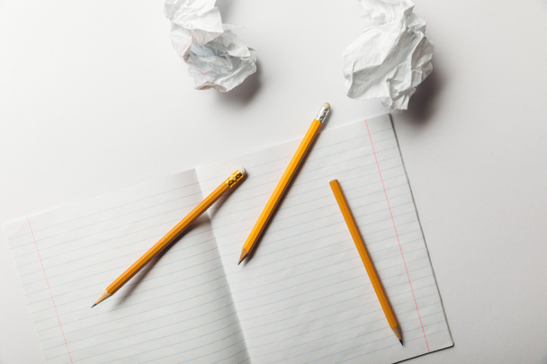верхний вид чистого листа, лежащего рядом с мятой бумаги и карандашей на белом фоне
  - Фото, изображение