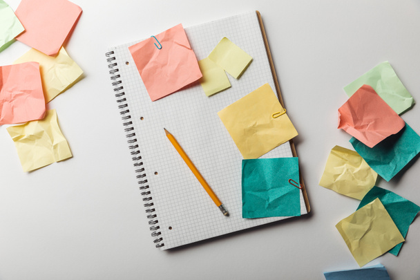 top view of notebook with blank squared page near crumpled colorful sticky notes on white background - Photo, Image