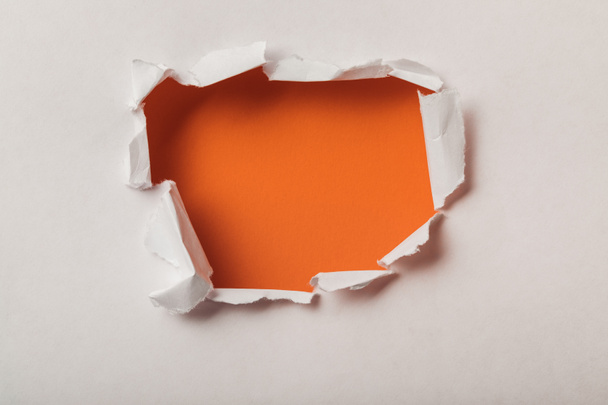torn hole in sheet of paper on orange background - Photo, Image
