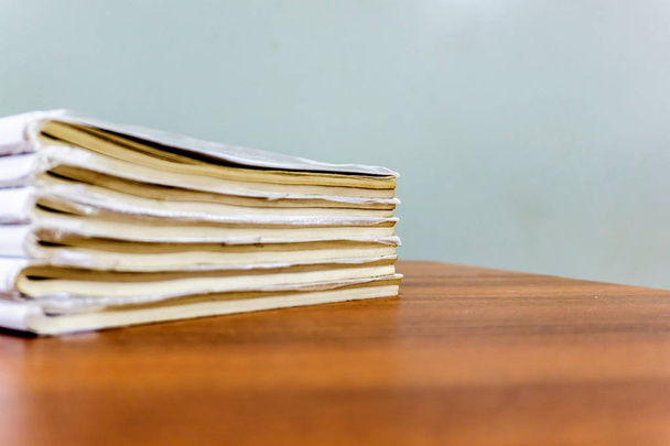 Une pile de livres est couchée sur une table brune, les documents sont empilés en gros plan
 - Photo, image