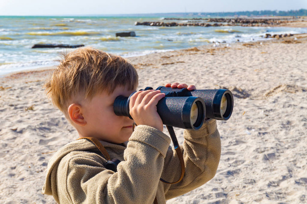 O menino olha através de binóculos na praia
 - Foto, Imagem