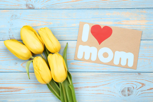 Greeting card with text I Love Mom and yellow tulips on wooden table - Fotografie, Obrázek