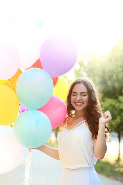 Beautiful girl with colored balloons in the park - 写真・画像