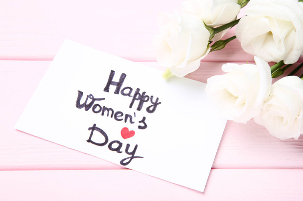 Text Happy Women's Day with eustoma flowers on pink wooden table - Photo, image