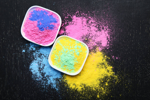 Colorful holi powder in bowls on black wooden table - Фото, изображение