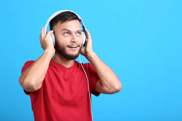 Young man with headphones on blue background - 写真・画像