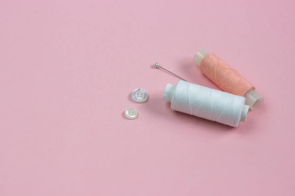 white and pink threads, white buttons and a needle on a pink background - Valokuva, kuva