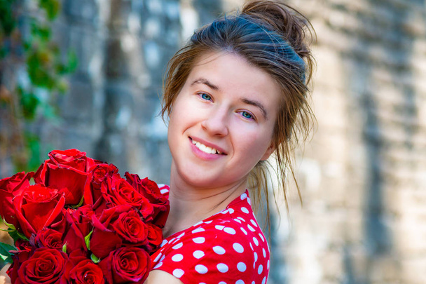 Hermosa y sexy chica con un ramo de rosas rojas se encuentra en el fondo de una vieja pared de ladrillo
 - Foto, Imagen