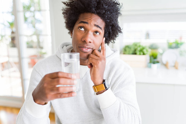 Hombre afroamericano bebiendo un vaso de agua en casa cara seria pensando en la pregunta, idea muy confusa
 - Foto, imagen