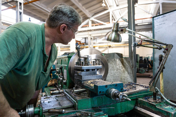 Lavoratore, un uomo elabora prodotti metallici su una macchina. Tornitura del lavoro in produzione
 - Foto, immagini