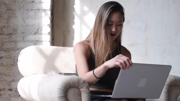 junge Frau sitzt Sessel Büroeinrichtung mit Laptop-Computer und Smartphone drahtlose Technologie, drahtlose Kommunikation, Remote-Arbeitskonzept - Filmmaterial, Video