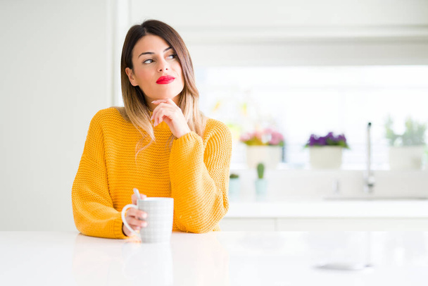 Jovem mulher bonita bebendo uma xícara de café em casa rosto sério pensando em questão, ideia muito confusa
 - Foto, Imagem