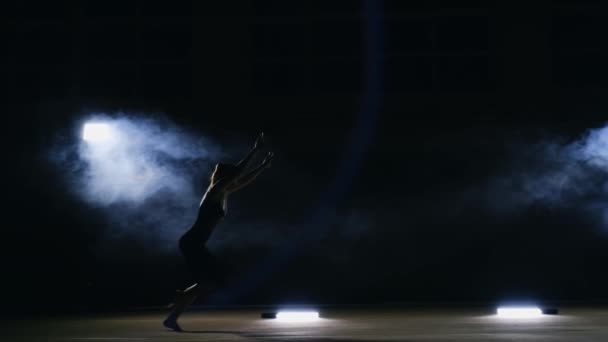 Die talentierte Turnerin vollführt in Zeitlupe einen Salto in einem Sprung auf dem Turnteppich in einem konturierten Licht im Rauch. Schwebestativ. die Rotation in der Luft. Akrobatik - Filmmaterial, Video