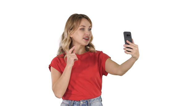 Cheerful female blogger recording video to front camera of modern telephone while walking on white background. - Foto, afbeelding