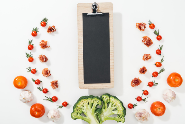 top view of clipboard among tomatoes, leaves, broccoli, prosciutto and garlic - Photo, Image