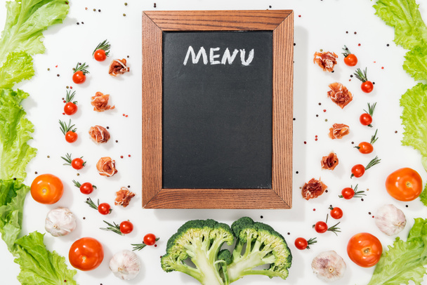 vista dall'alto del pannello di gesso con scritte di menu tra pomodori, foglie di lattuga, prosciutto, broccoli, spezie e aglio
 - Foto, immagini