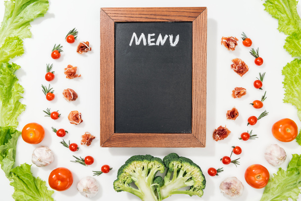 vista superior de pizarra con letras de menú entre tomates, hojas de lechuga, jamón, brócoli y ajo
 - Foto, Imagen