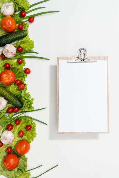 top view of clipboard with tomatoes, lettuce leaves, cucumbers, onion and garlic - 写真・画像