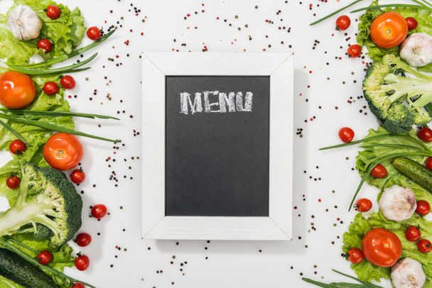bovenaanzicht van krijt bord met menu belettering onder tomaten, sla bladeren, komkommer, ui, kruiden en knoflook - Foto, afbeelding