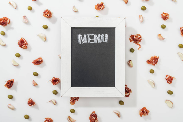 top view of chalk board with menu lettering among prosciutto, olives and garlic cloves - Zdjęcie, obraz