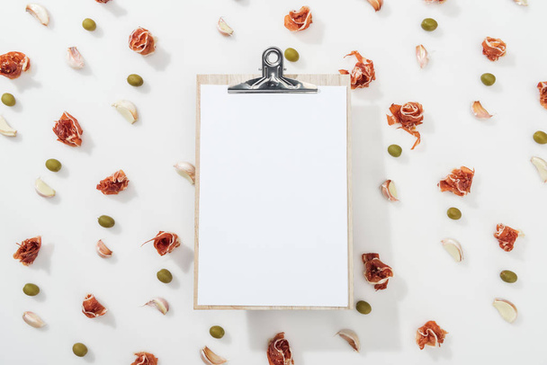top view of empty clipboard among prosciutto, olives and garlic cloves - Photo, Image