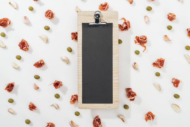top view of blank clipboard among prosciutto, olives and garlic cloves - Foto, afbeelding