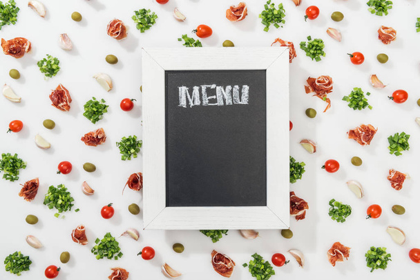 vista superior de pizarra con letras de menú entre prosciutto, aceitunas, dientes de ajo, vegetación y tomates cherry
 - Foto, imagen