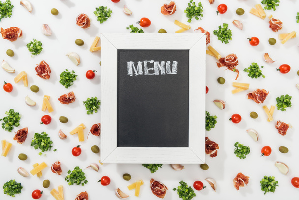 bovenaanzicht van krijt bord met menu belettering onder olijven, prosciutto, groen, gesneden kaas, knoflookteentjes en kerstomaatjes - Foto, afbeelding