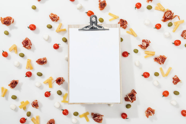 white clipboard among olives, prosciutto, mozzarella, cut cheese and cherry tomatoes - Photo, Image