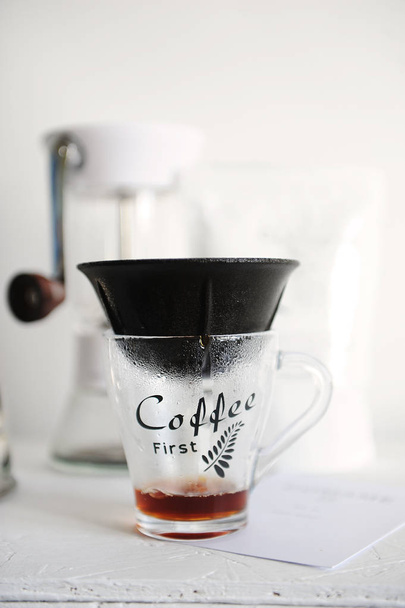 Alternatieve handmatige koffie brouwen in poreuze keramische immateriële japan dripper filter op de kop met een inscriptie koffie eerst. Handmatige koffiemolen. Witte achtergrond. - Foto, afbeelding