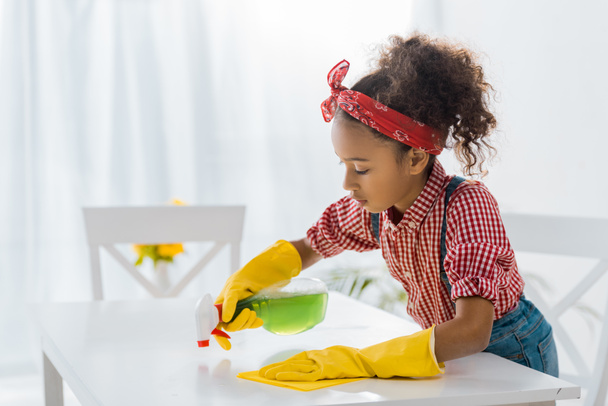 cute african american child in yellow rubber gloves washing table with cleaning spray and rag - Valokuva, kuva