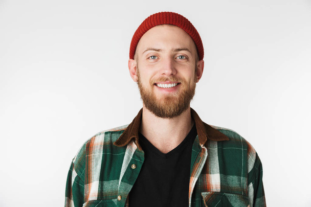 Portrait of stylish bearded guy wearing hat and plaid shirt smiling while standing isolated over white background - Foto, imagen