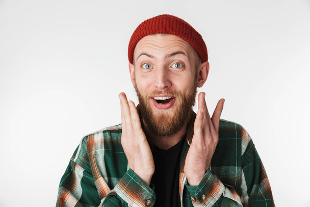 Portrait of handsome bearded guy wearing hat and plaid shirt smiling while standing isolated over white background - Photo, image