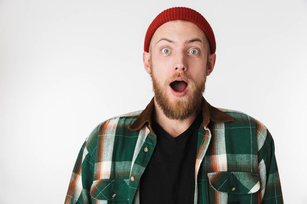 Portrait of excited bearded guy wearing hat and plaid shirt smiling while standing isolated over white background - Photo, image