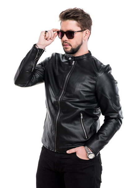Young beard man in sunglasses wearing black leather jacket posing in studio - 写真・画像