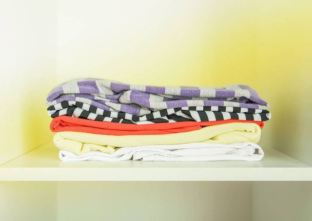 Montón de ropa de diferentes colores en estante de armario de madera blanca
. - Foto, imagen