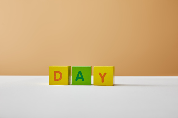 day lettering made of multicolored blocks on white table and beige background - Valokuva, kuva