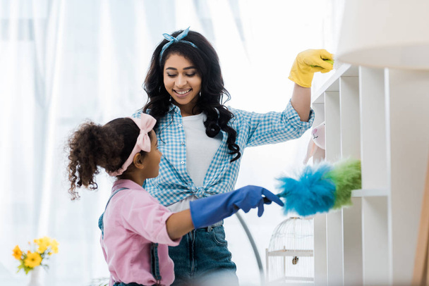 sorridente afro-americano mãe e filha limpeza prateleiras com espanadores
 - Foto, Imagem