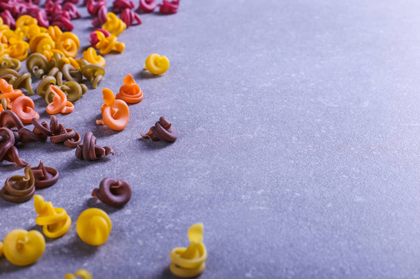 Multicolored pasta of unusual shape with natural vegetable dyes, scattered on table. Background closeup. - Foto, Bild