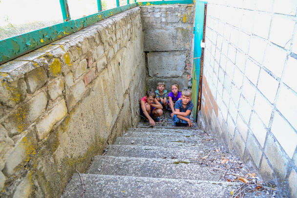 Kinder im Keller, drei Jungen und ein Mädchen in der Nähe der Eisentür verstecken sich auf den Stufen vor der Außenwelt. Postproduktionsfoto. - Foto, Bild
