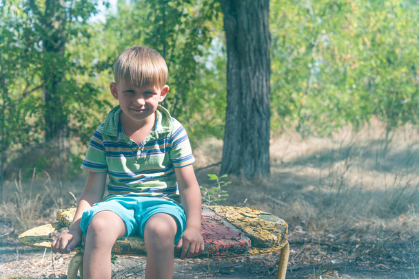 Çocuk terkedilmiş Parkı içinde eski bir bankta oturur ve üzgün bir yüz ile etrafına bakıyor. - Fotoğraf, Görsel