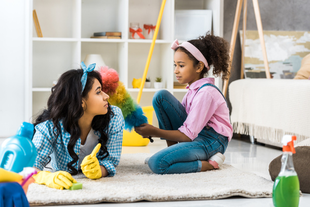 cute african american child with multicolored duster sitting on carpet while mother lying near - 写真・画像