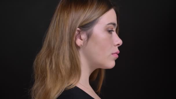Closeup portrait of young attractive caucasian female turning and looking at camera with background isolated on black - Filmagem, Vídeo